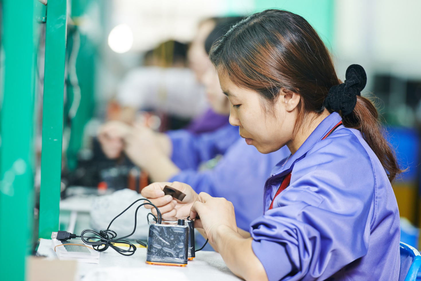 Asiatische Frau arbeitet in einer Manufaktur an einem elektronischen Gerät; Kurtz Detektei Nürnberg