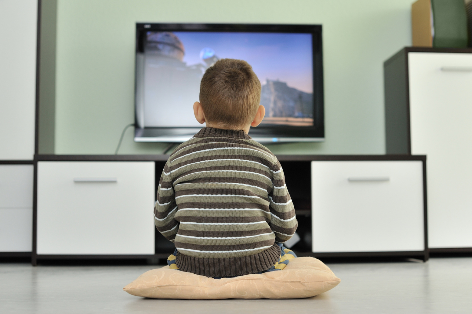 Kleiner Junge sitzt allein auf einem Kissen auf dem Fußboden vor einem Fernseher; Sorgerecht, Kurtz Detektei Nürnberg.